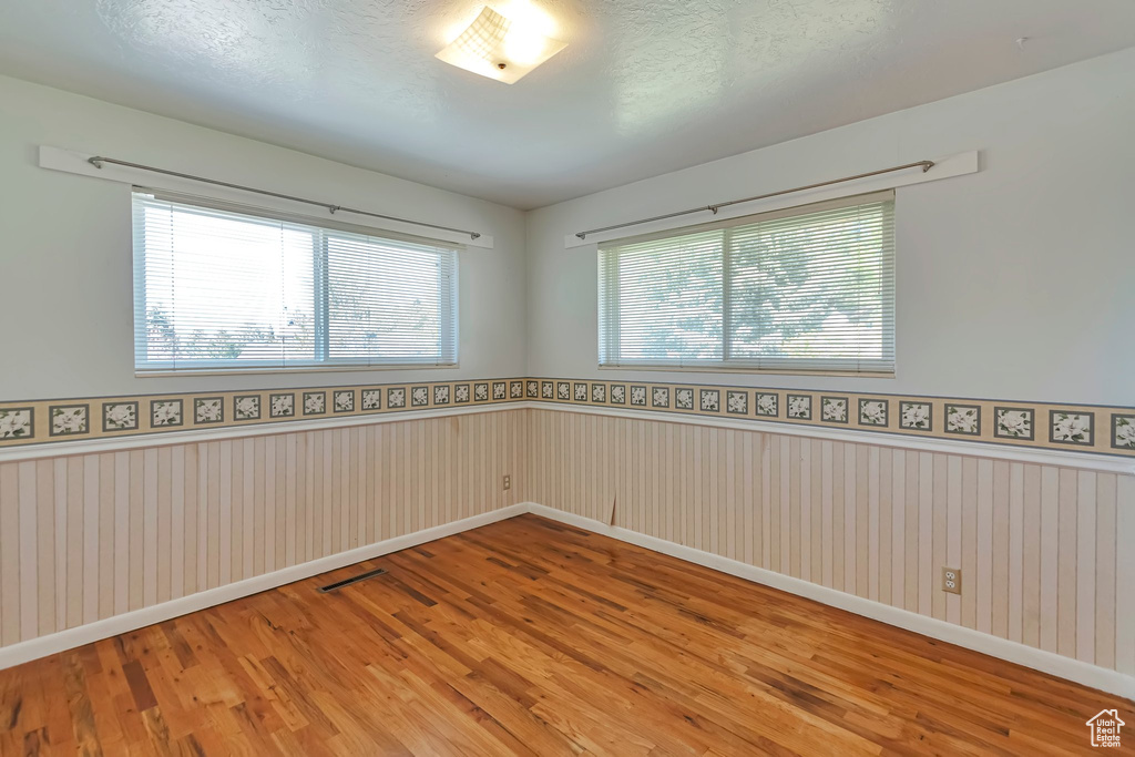 Empty room featuring wood finished floors, healthy amount of natural light, wainscoting, and baseboards