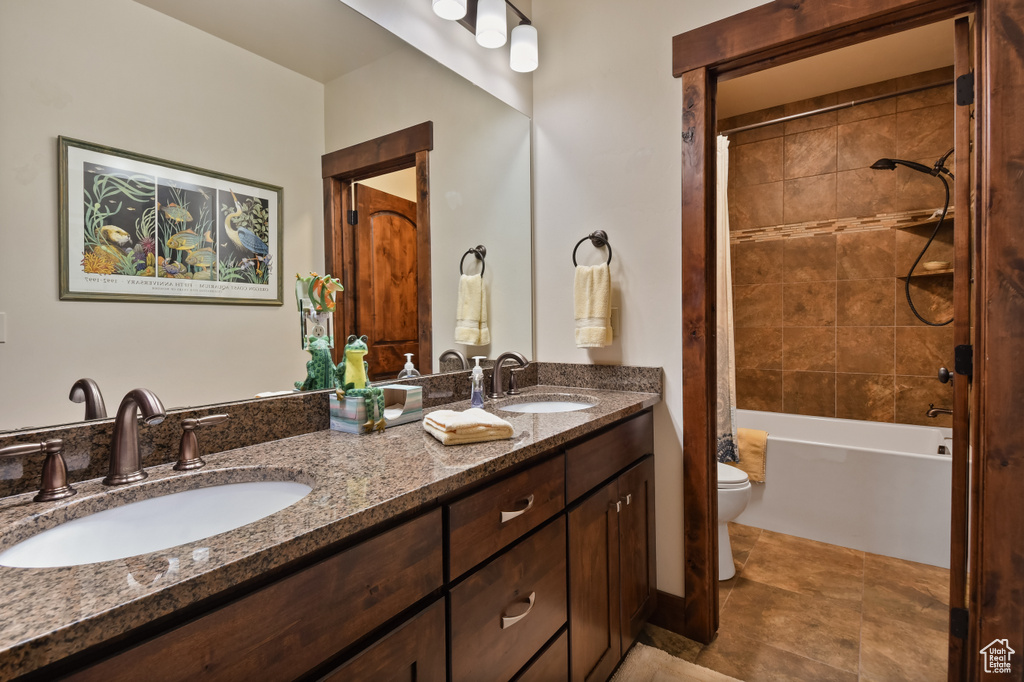Bathroom featuring toilet, double vanity, and shower / bath combination with curtain