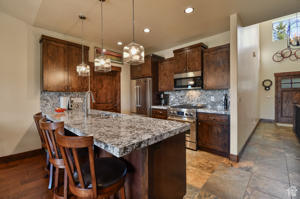 Kitchen with high end appliances, a sink, baseboards, a peninsula, and decorative backsplash