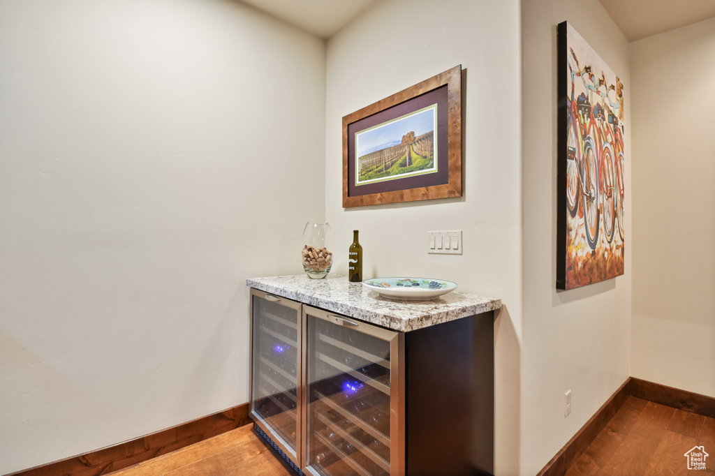 Indoor dry bar with wood finished floors, baseboards, and beverage cooler