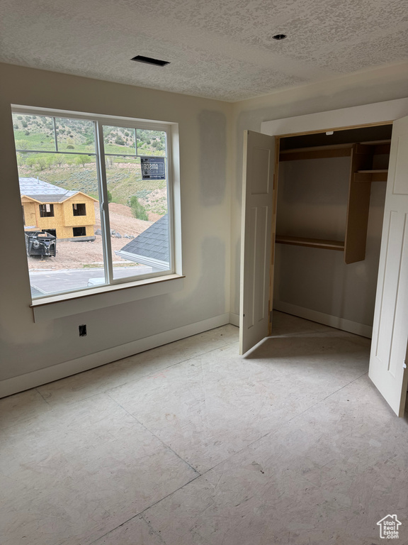 Unfurnished bedroom featuring multiple windows, baseboards, a textured ceiling, and a closet