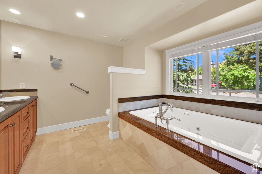 Bathroom featuring healthy amount of natural light, a whirlpool tub, baseboards, double vanity, and recessed lighting