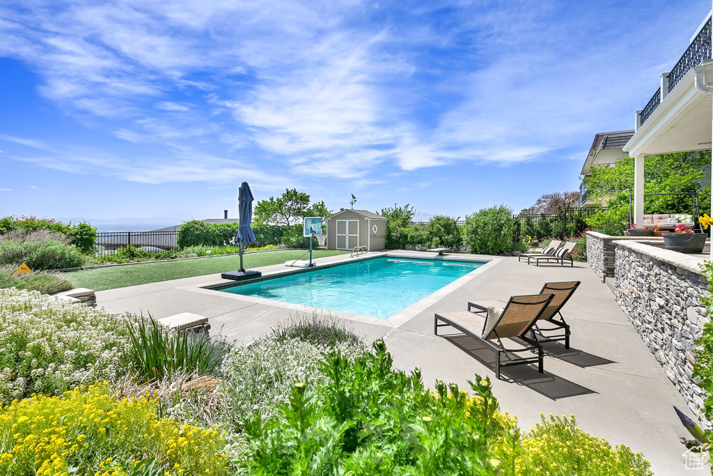 View of swimming pool with a patio, a shed, fence, an outdoor structure, and a diving board