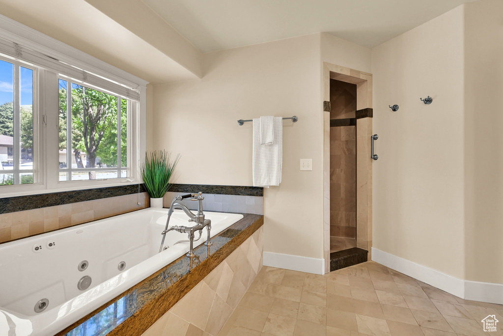 Bathroom with a tub with jets, baseboards, and a tile shower