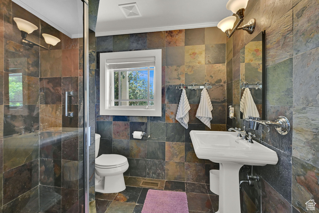 Full bathroom featuring tile walls, a shower stall, crown molding, toilet, and stone finish flooring
