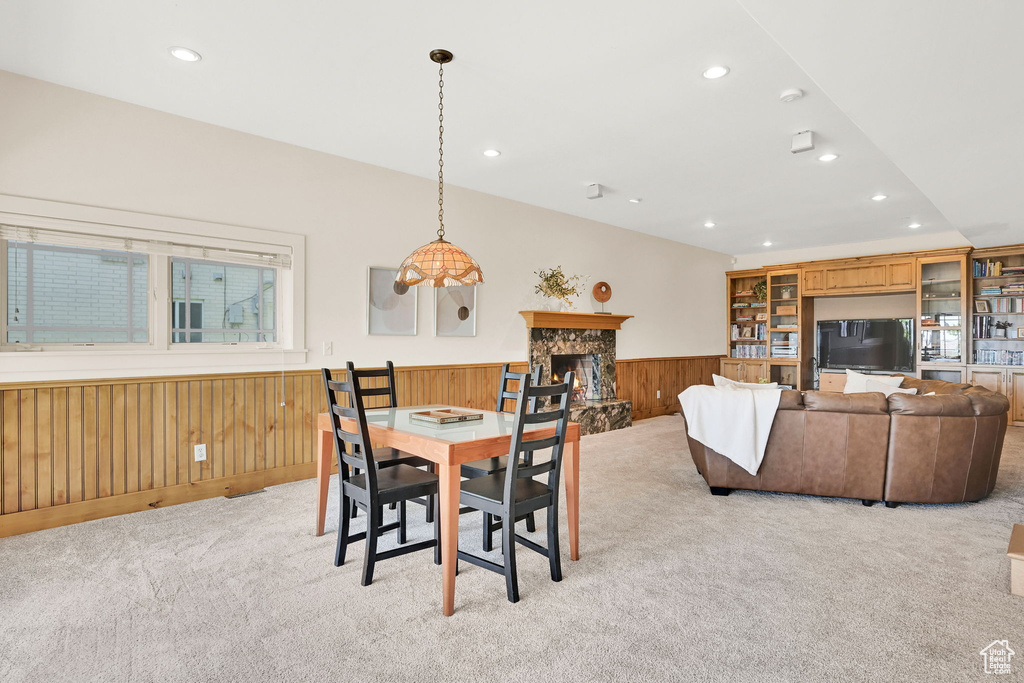 Dining space with light colored carpet, wainscoting, recessed lighting, a stone fireplace, and wood walls