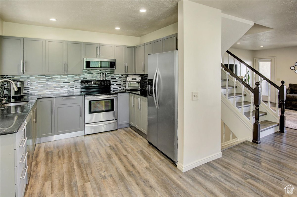 Kitchen with appliances with stainless steel finishes, gray cabinets, light wood-type flooring, a textured ceiling, and recessed lighting