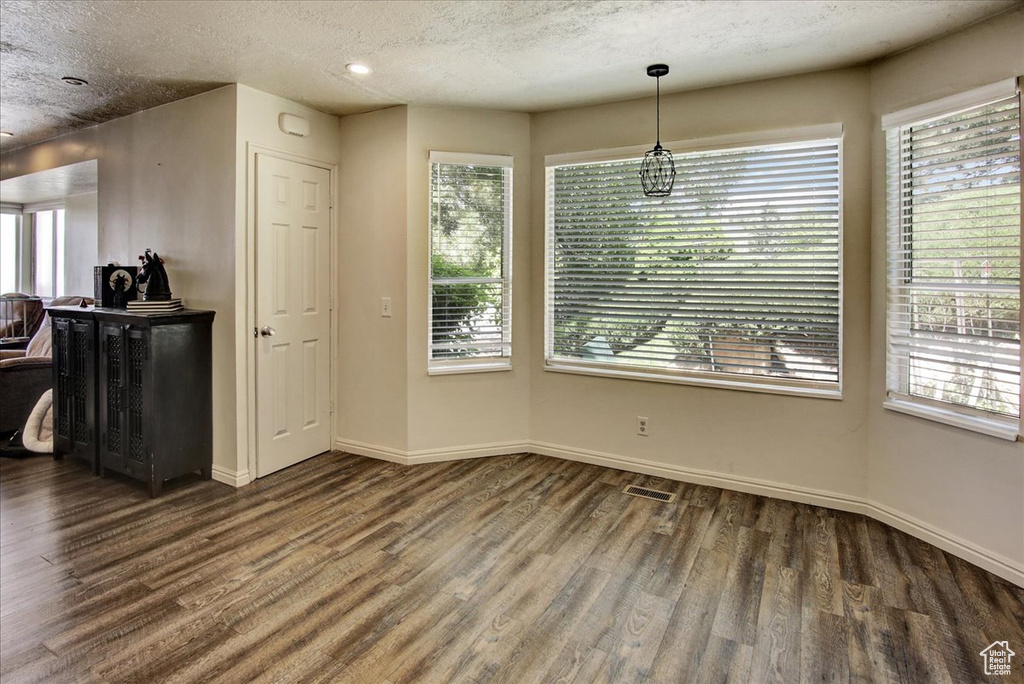 Unfurnished dining area with wood finished floors, plenty of natural light, baseboards, and a textured ceiling