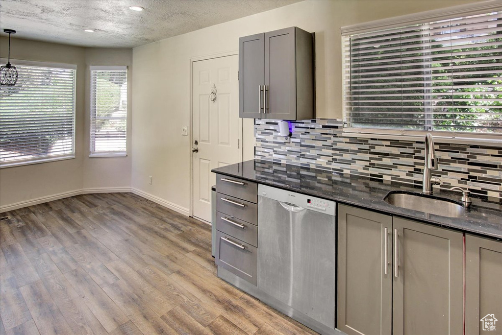Kitchen featuring stainless steel dishwasher, gray cabinets, tasteful backsplash, a sink, and light wood finished floors