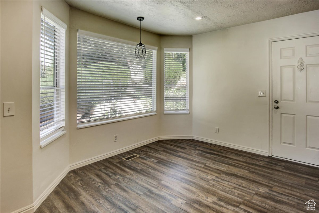 Unfurnished dining area with plenty of natural light, dark wood-type flooring, a textured ceiling, baseboards, and recessed lighting