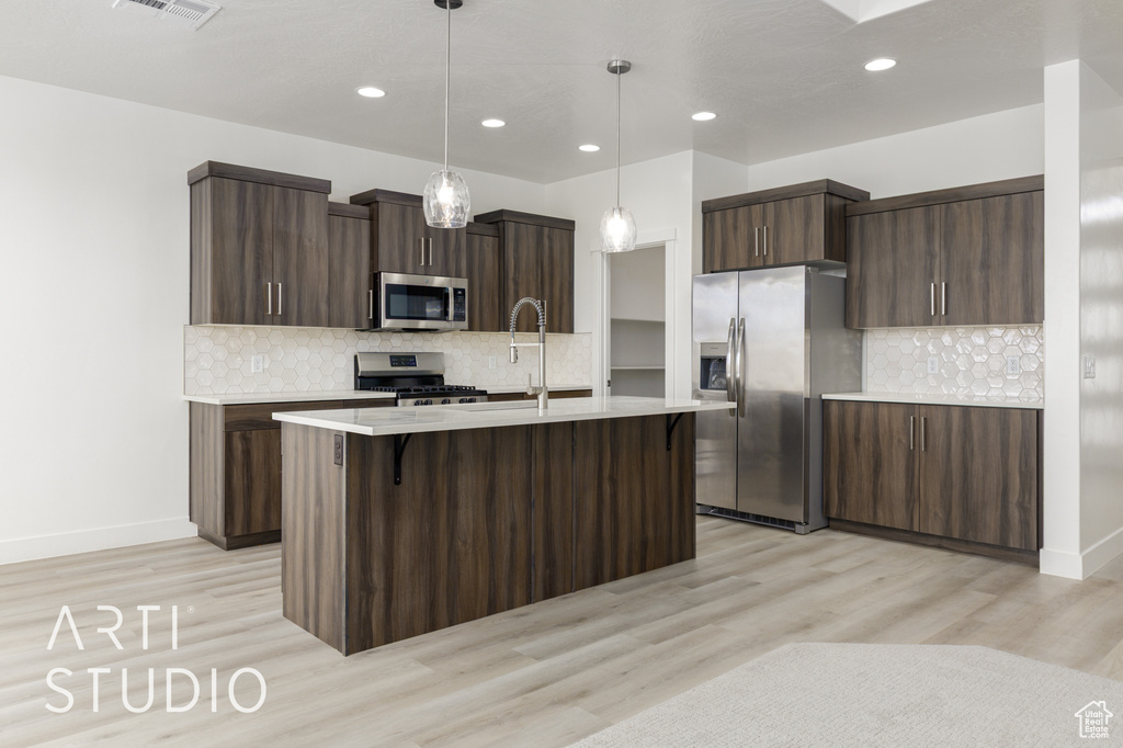 Kitchen featuring appliances with stainless steel finishes, light countertops, decorative backsplash, light wood-style flooring, and recessed lighting