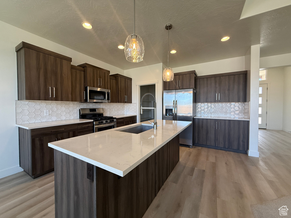 Kitchen with stainless steel appliances, light wood-style floors, dark brown cabinetry, a sink, and backsplash