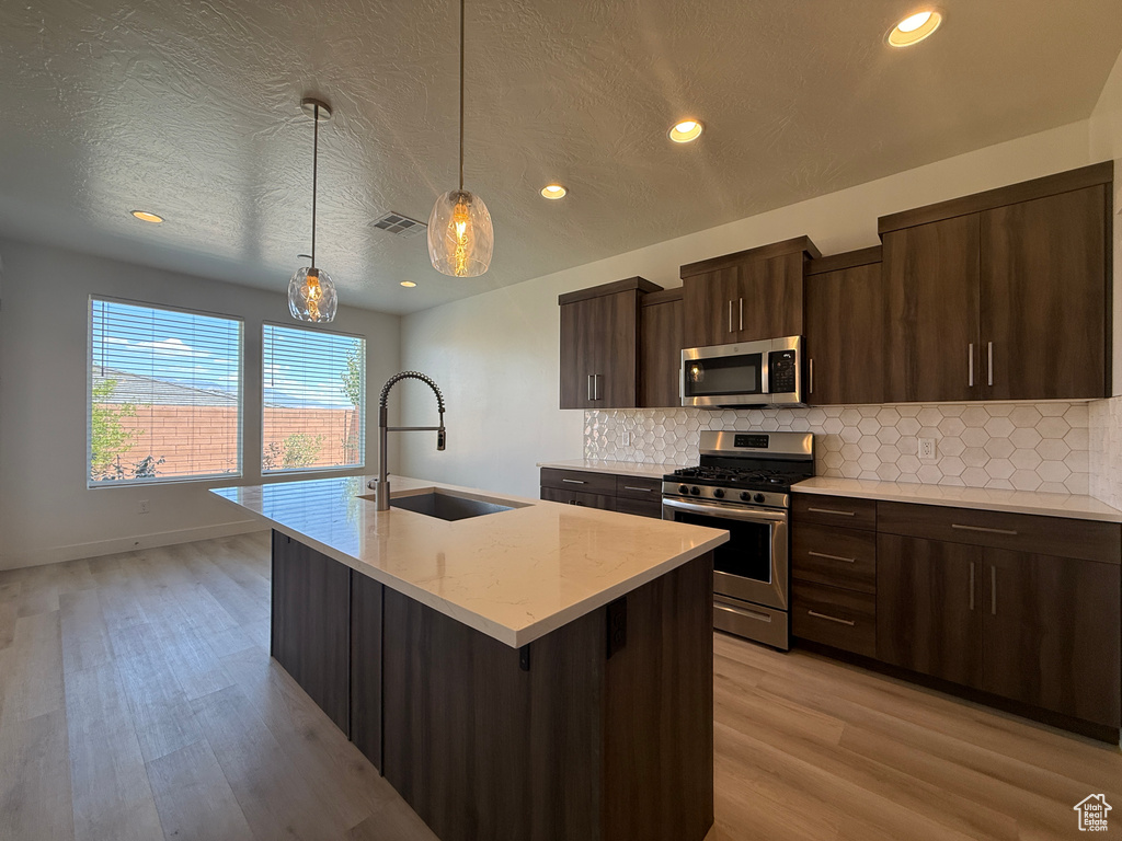 Kitchen featuring appliances with stainless steel finishes, a sink, tasteful backsplash, light wood-style floors, and recessed lighting