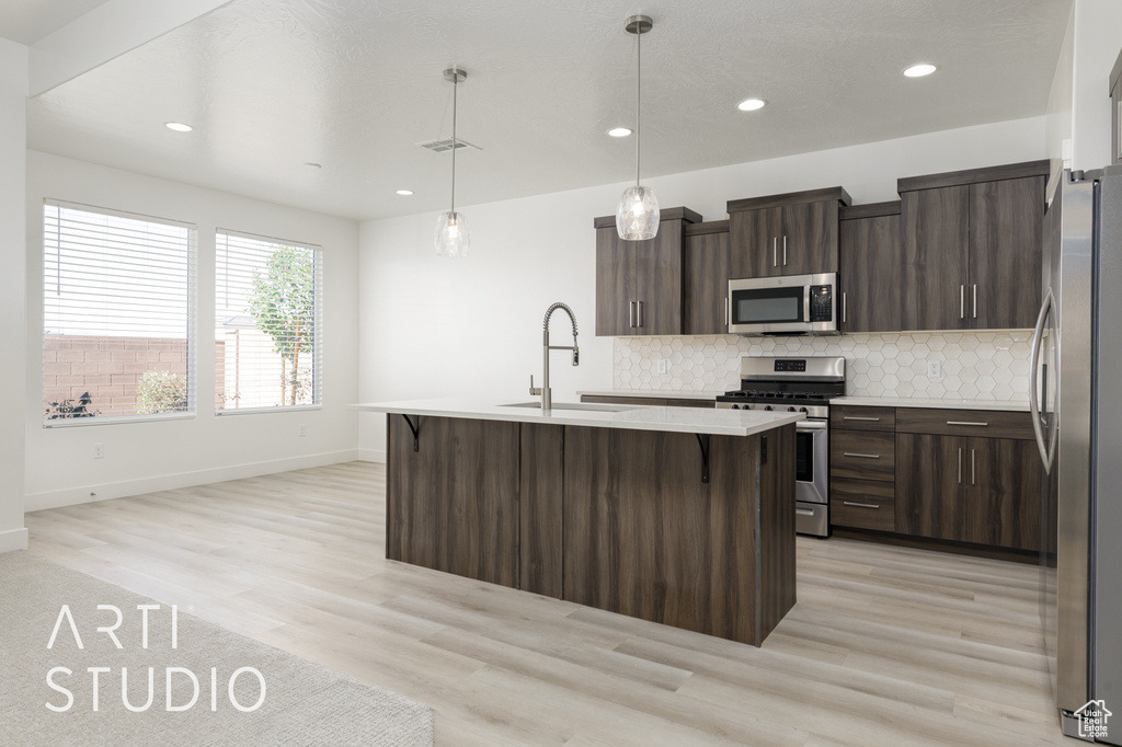 Kitchen with appliances with stainless steel finishes, a sink, baseboards, light countertops, and backsplash