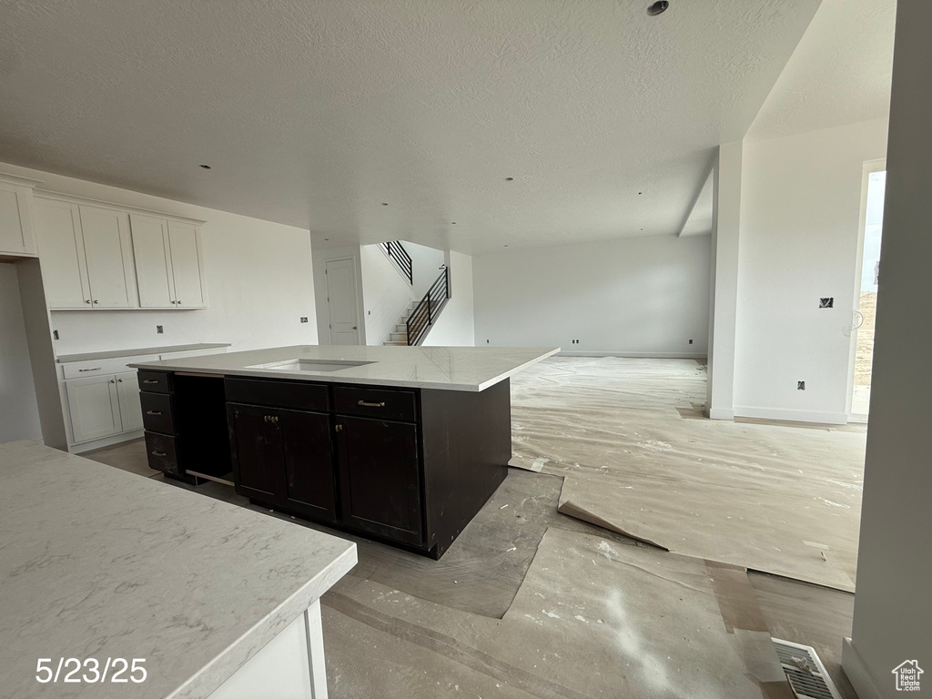 Kitchen with open floor plan, a kitchen island, stovetop, dark cabinetry, and white cabinets