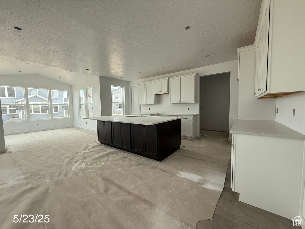 Kitchen featuring a textured ceiling, a center island, lofted ceiling, white cabinetry, and light countertops