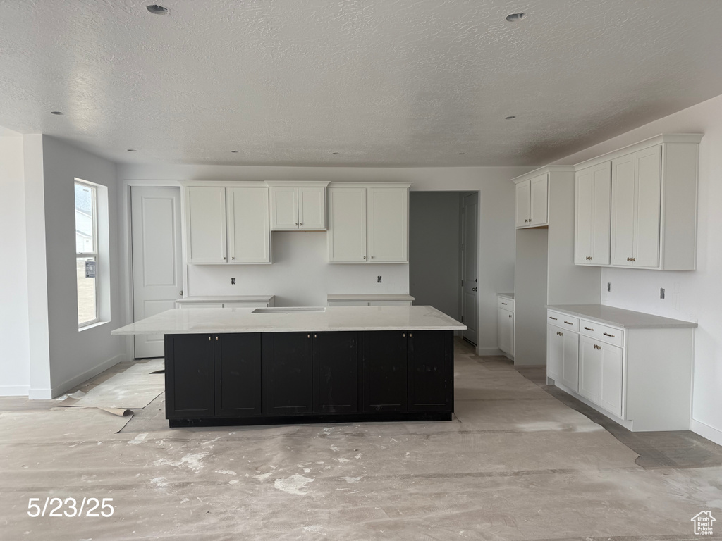 Kitchen with baseboards, white cabinets, a spacious island, and a textured ceiling