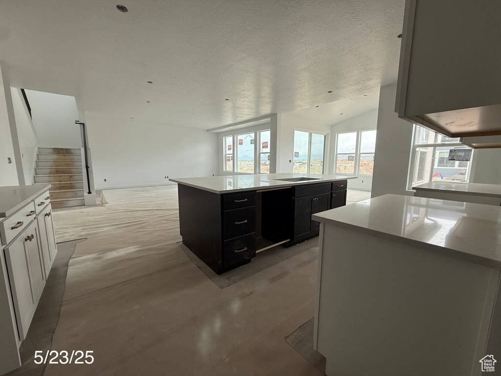 Kitchen featuring a center island, open floor plan, dark cabinetry, vaulted ceiling, and concrete floors