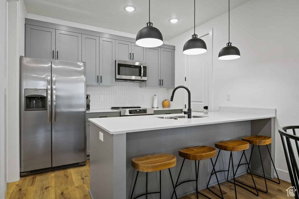Kitchen featuring appliances with stainless steel finishes, a sink, gray cabinetry, a breakfast bar, and backsplash