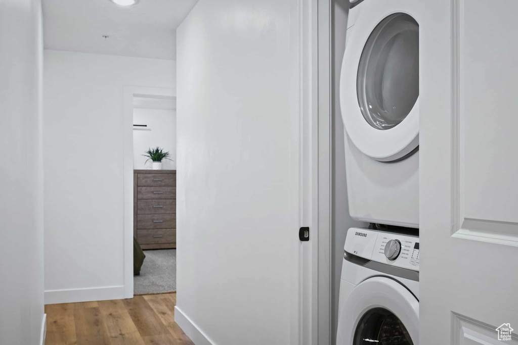 Laundry area with stacked washer / drying machine, wood finished floors, and baseboards