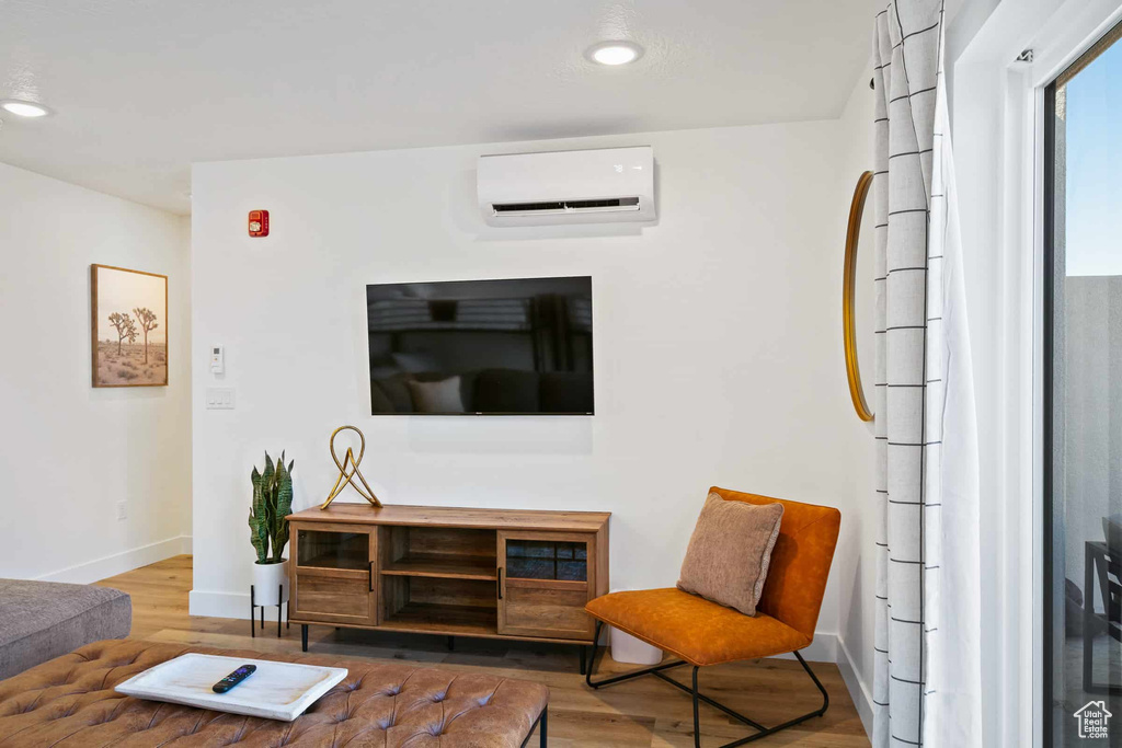 Living area with a wall mounted air conditioner, wood finished floors, baseboards, and recessed lighting