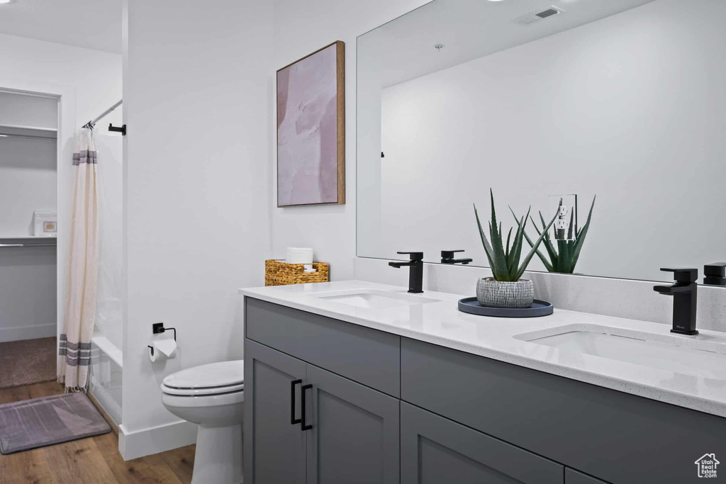 Bathroom featuring wood finished floors, toilet, double vanity, and baseboards