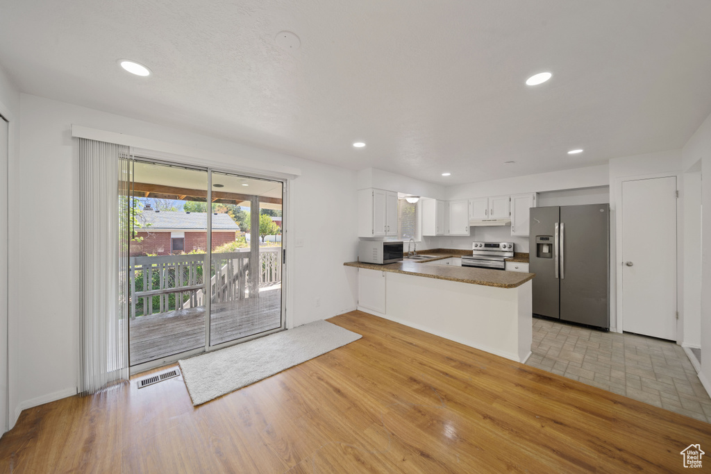 Kitchen with appliances with stainless steel finishes, a peninsula, under cabinet range hood, dark countertops, and white cabinets