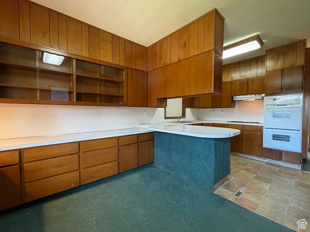 Kitchen featuring white appliances, under cabinet range hood, open shelves, a sink, and brown cabinetry