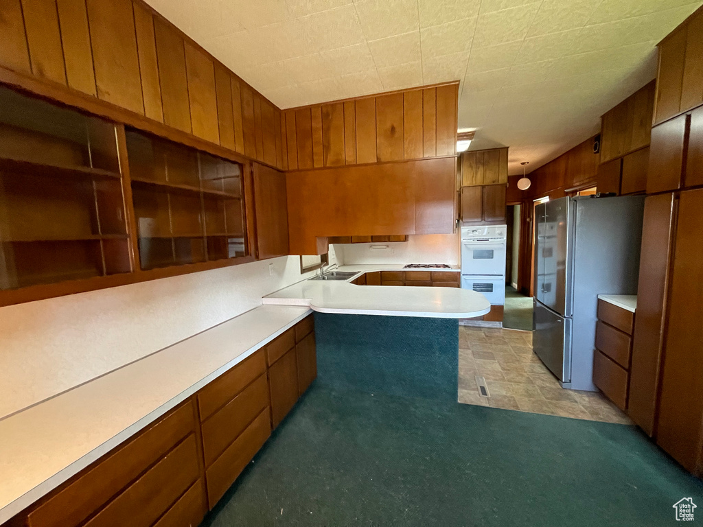 Kitchen with freestanding refrigerator, double oven, brown cabinets, light countertops, and a sink