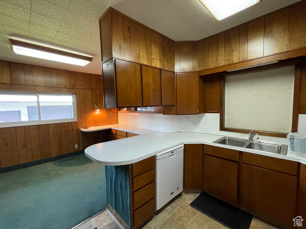 Kitchen featuring white dishwasher, a sink, light countertops, wooden walls, and a peninsula