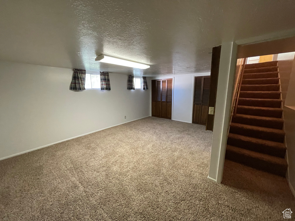 Below grade area featuring stairway, carpet flooring, baseboards, and a textured ceiling