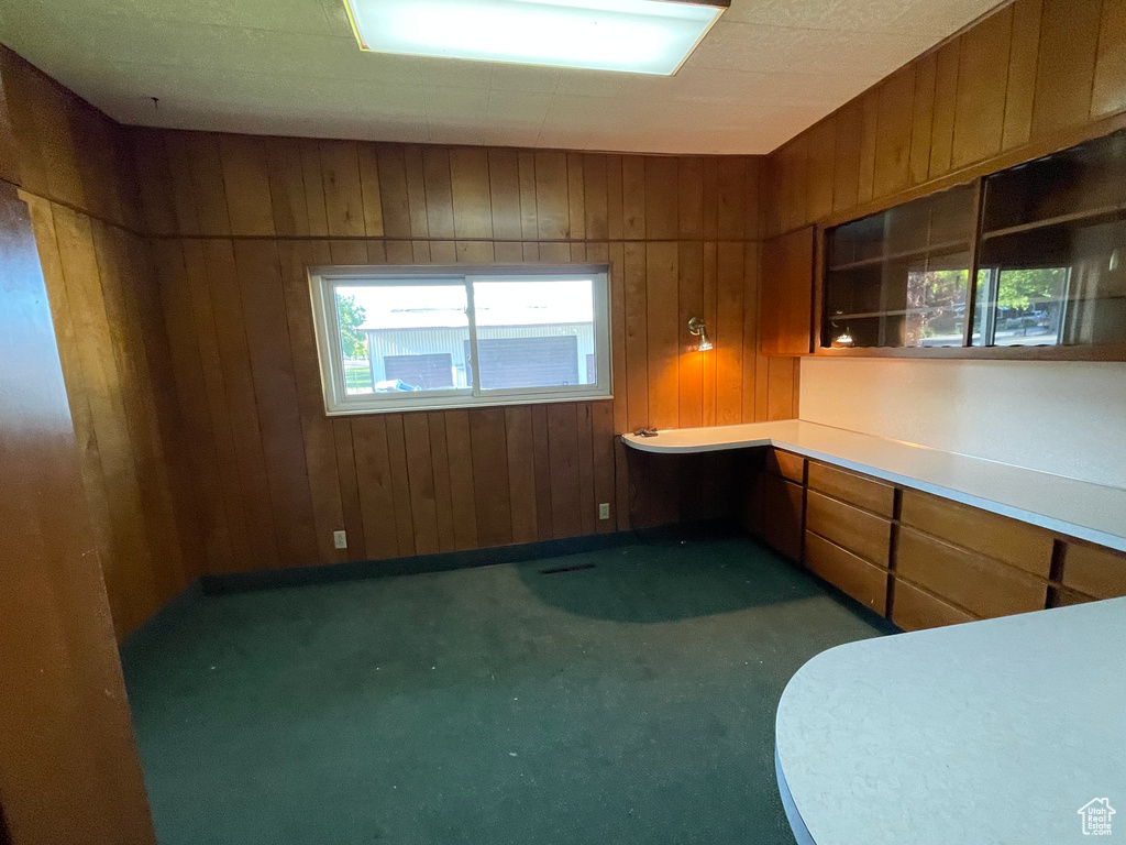 Kitchen with wood walls, brown cabinetry, carpet flooring, and light countertops