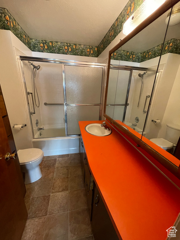 Bathroom featuring toilet, double vanity, bath / shower combo with glass door, and a textured ceiling