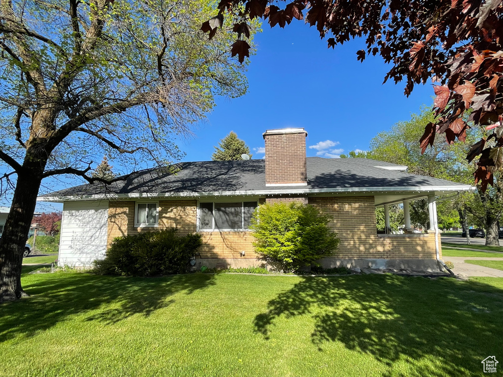 Rear view of property with brick siding, a yard, a chimney, and roof with shingles