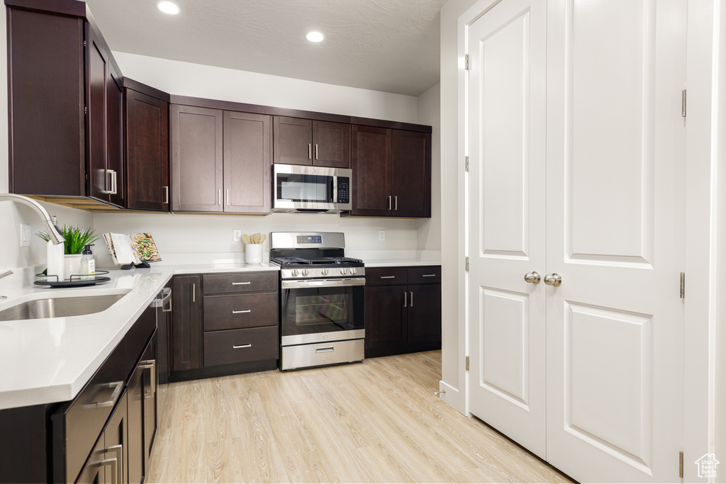 Kitchen featuring stainless steel appliances, a sink, light countertops, dark brown cabinetry, and recessed lighting