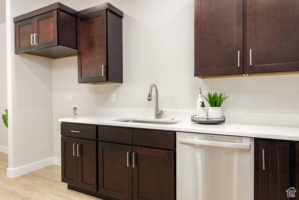 Kitchen with stainless steel dishwasher, a sink, light wood-type flooring, and dark brown cabinets