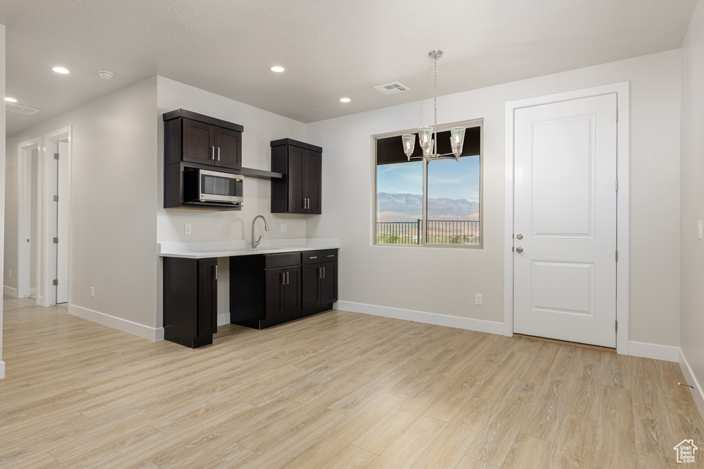 Kitchen featuring stainless steel microwave, light countertops, a chandelier, light wood-type flooring, and baseboards