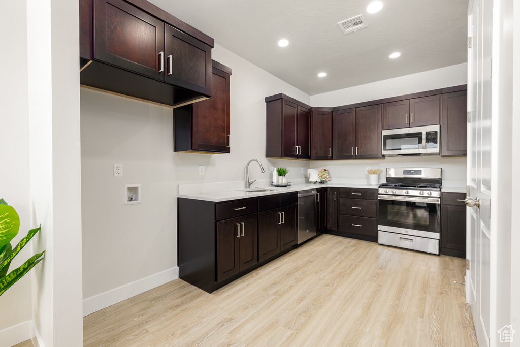 Kitchen featuring stainless steel appliances, a sink, light wood-style floors, recessed lighting, and dark brown cabinetry