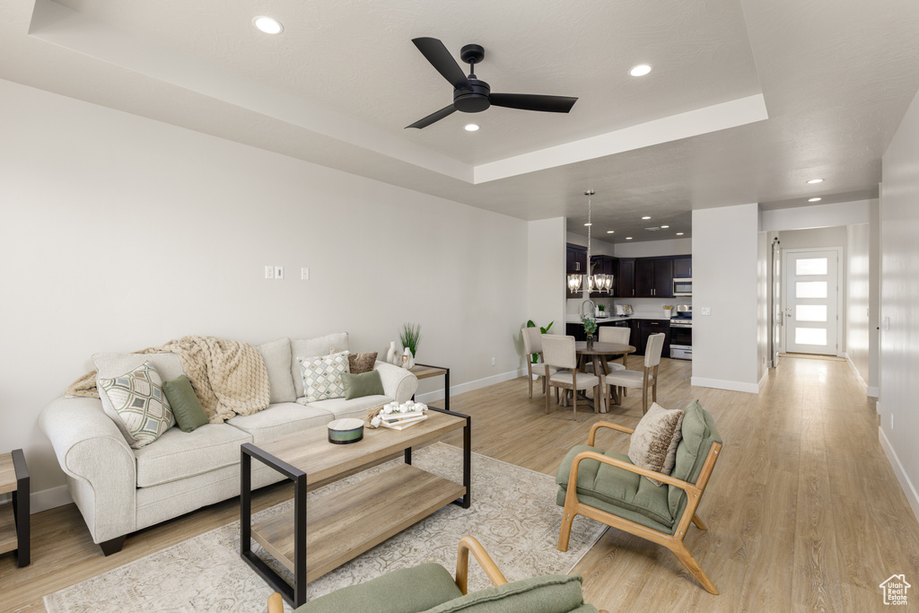 Living room featuring a tray ceiling, baseboards, ceiling fan, recessed lighting, and light wood-style floors