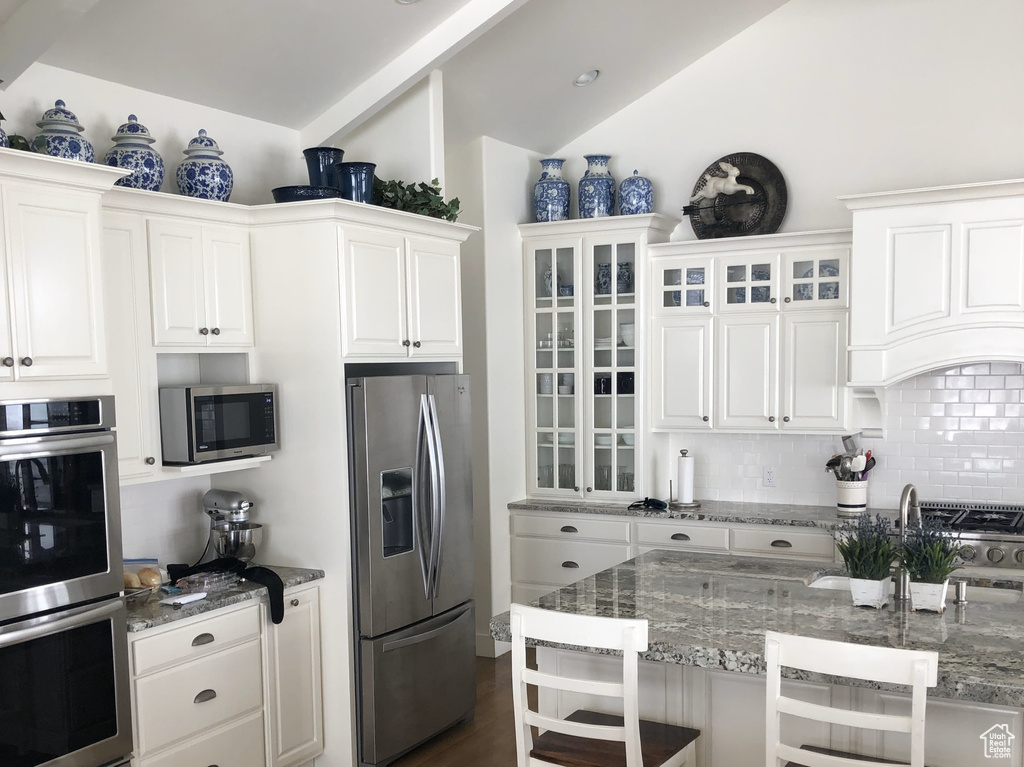 Kitchen with stainless steel appliances, backsplash, dark wood-style flooring, light stone countertops, and a kitchen breakfast bar
