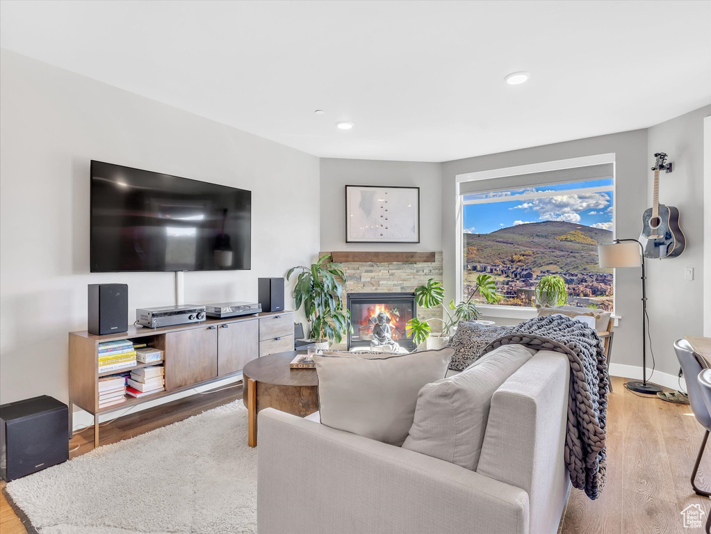 Living room with wood finished floors, a stone fireplace, recessed lighting, and baseboards