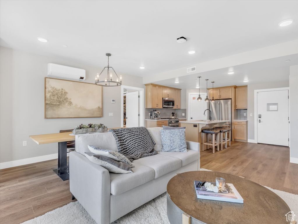 Living room with a chandelier, baseboards, a wall mounted AC, recessed lighting, and light wood-style flooring