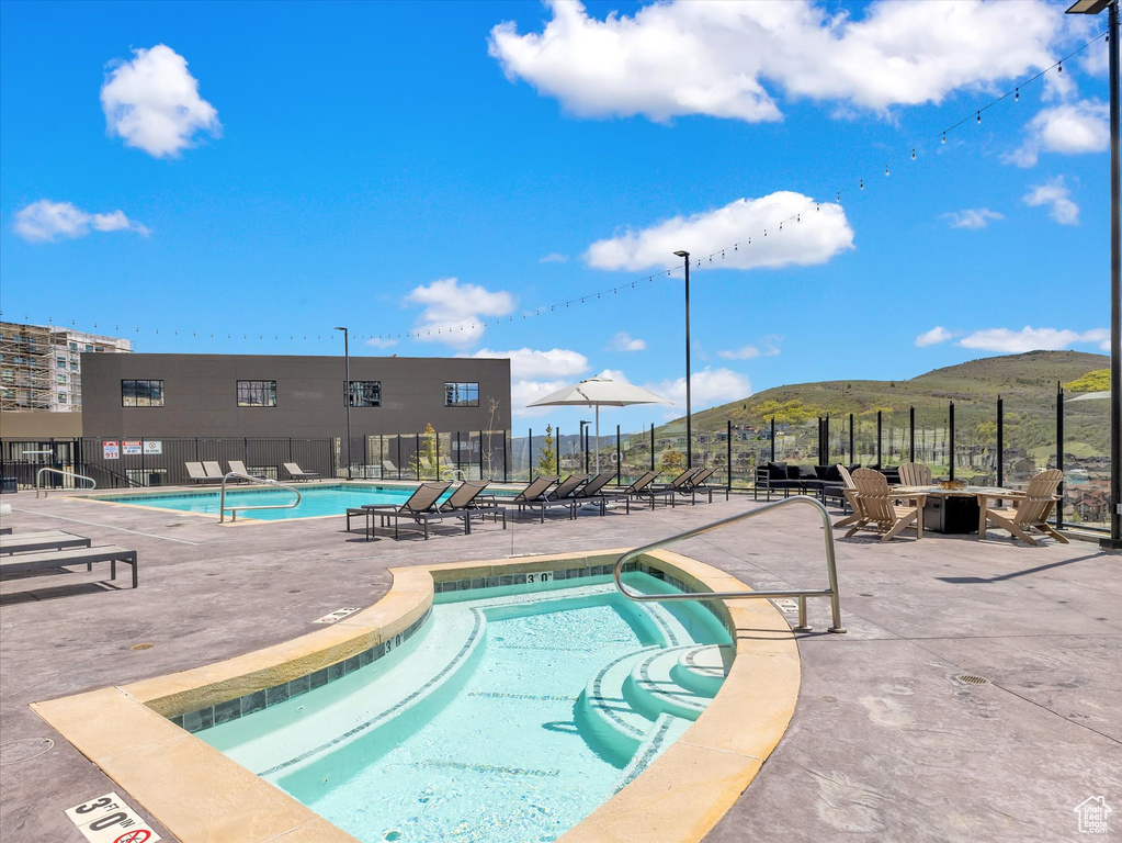 Community pool with fence, a mountain view, and a patio area