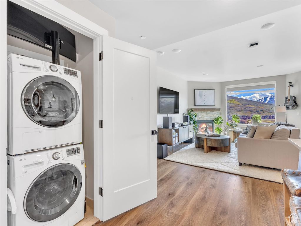 Clothes washing area with estacked washer and dryer, light wood-type flooring, a fireplace, and recessed lighting