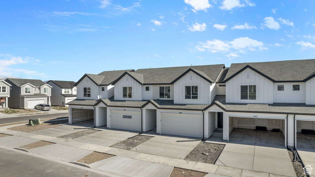 View of property with a residential view, board and batten siding, roof with shingles, an attached garage, and driveway