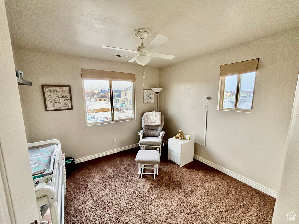Living area with plenty of natural light, ceiling fan, dark colored carpet, and baseboards