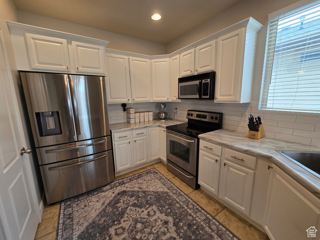 Kitchen featuring stainless steel appliances, backsplash, white cabinets, light tile patterned floors, and recessed lighting