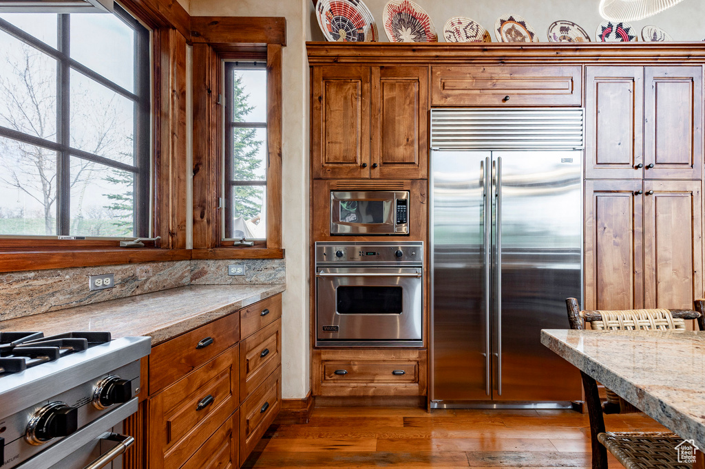 Kitchen with built in appliances, brown cabinetry, wood finished floors, and backsplash
