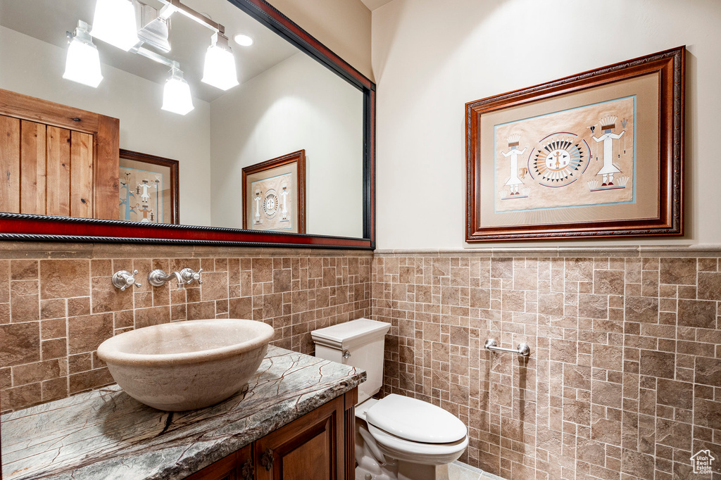 Bathroom with tile walls, toilet, wainscoting, and vanity