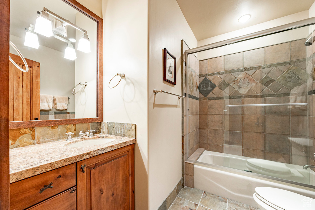 Full bath with bath / shower combo with glass door, baseboards, vanity, and toilet